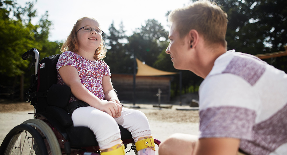 Ein Schulbegleiter mit einer Schülerin im Rollstuhl.