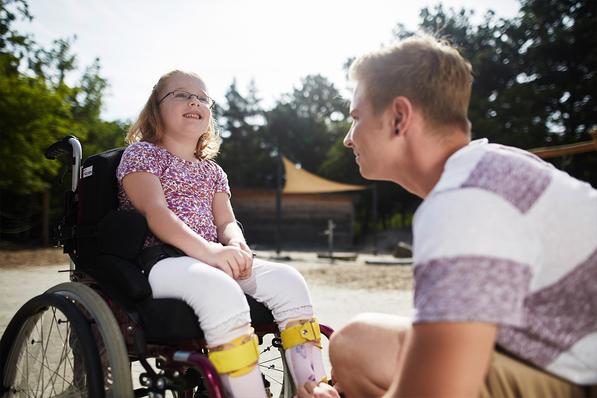 Ein Schulbegleiter mit einem Mädchen im Rollstuhl