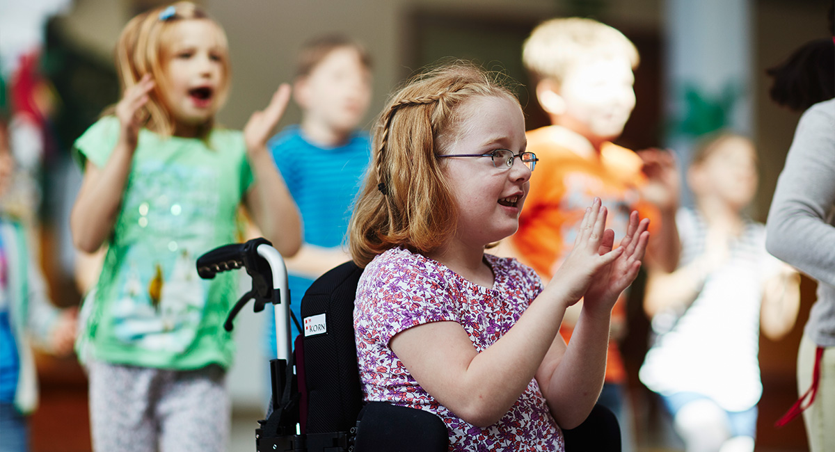 Ein Mädchen im Rollstuhl singt mit anderen Kindern im Kindergarten