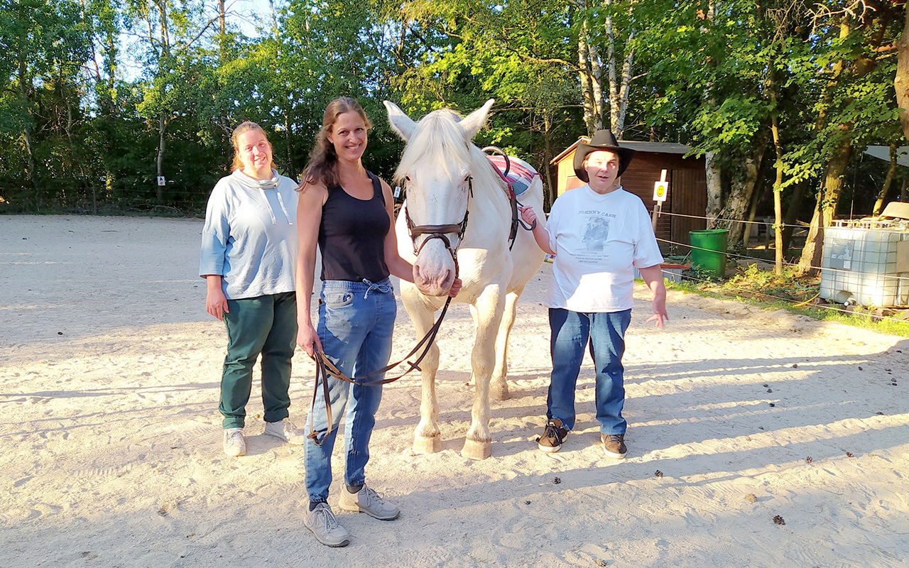 Eine Frau und zwei Menshen mit Behinderung bei der Reittherapie